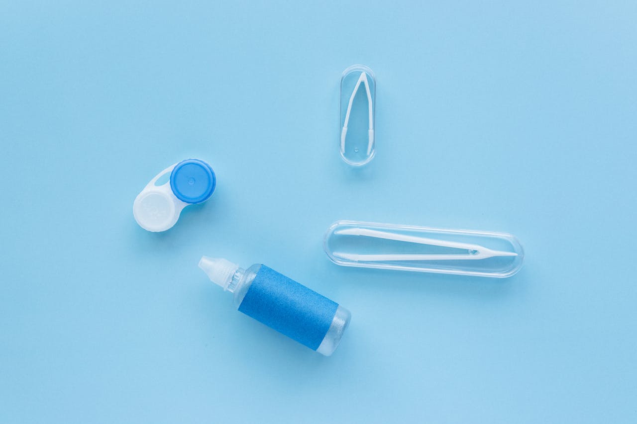 gallery-2 Flat lay of contact lens case, tweezers, and solution bottle on blue background.