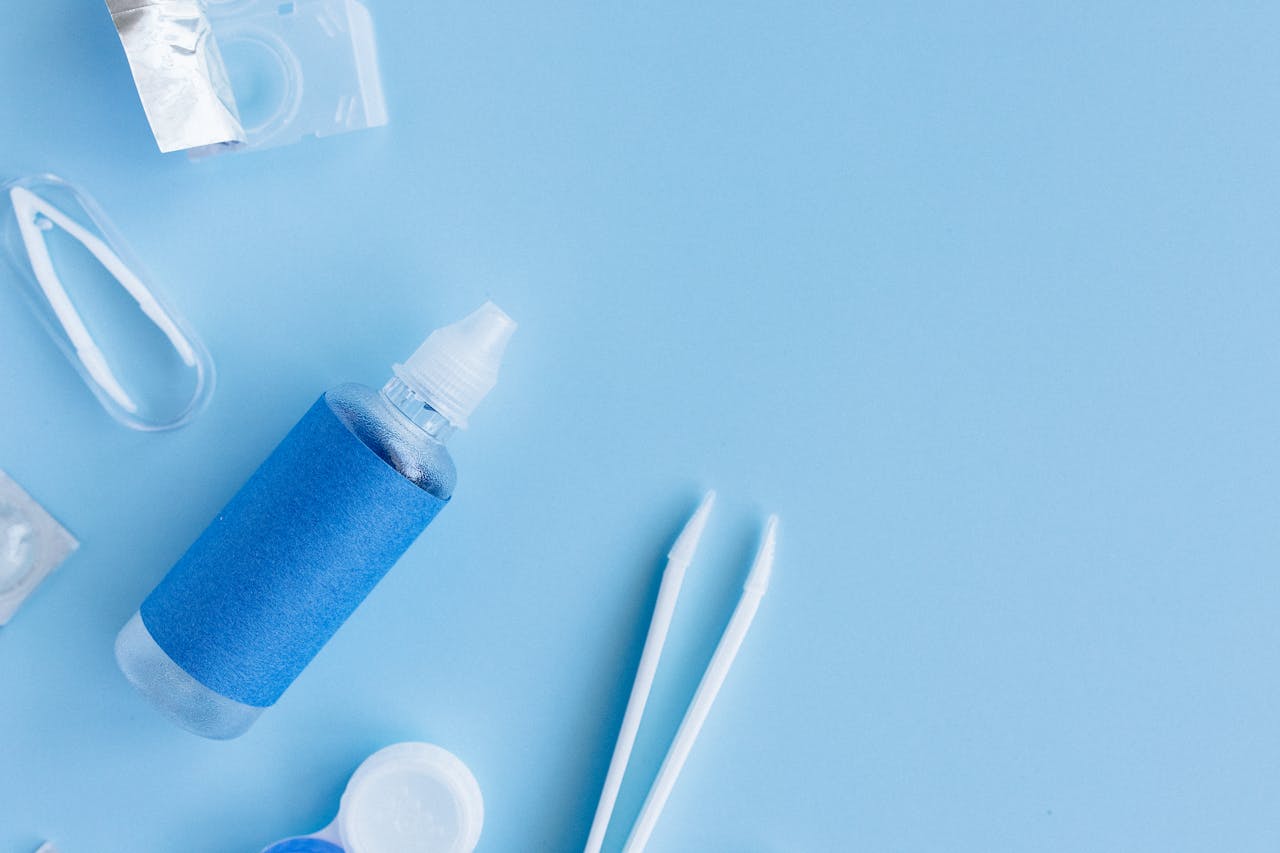 why-choose-us Flatlay of contact lens solution, case, and tweezers on blue background for eye care essentials.